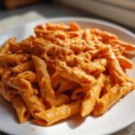 A serving of vibrant orange Creamy Roasted Red Pepper Pasta tossed with penne noodles, presented on a white plate.