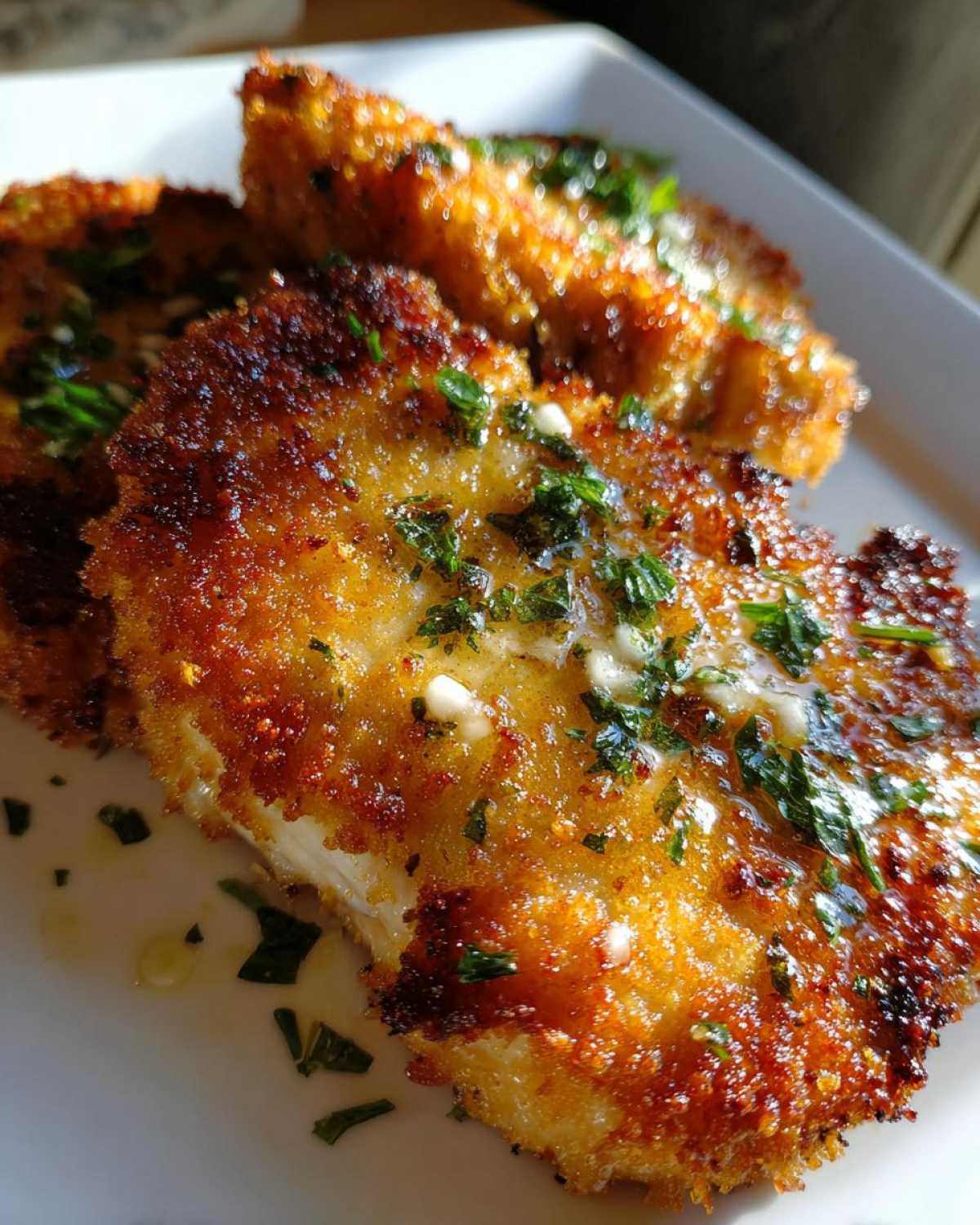 Close-up of crispy air fryer pork chops drizzled with melted garlic butter and fresh parsley.
