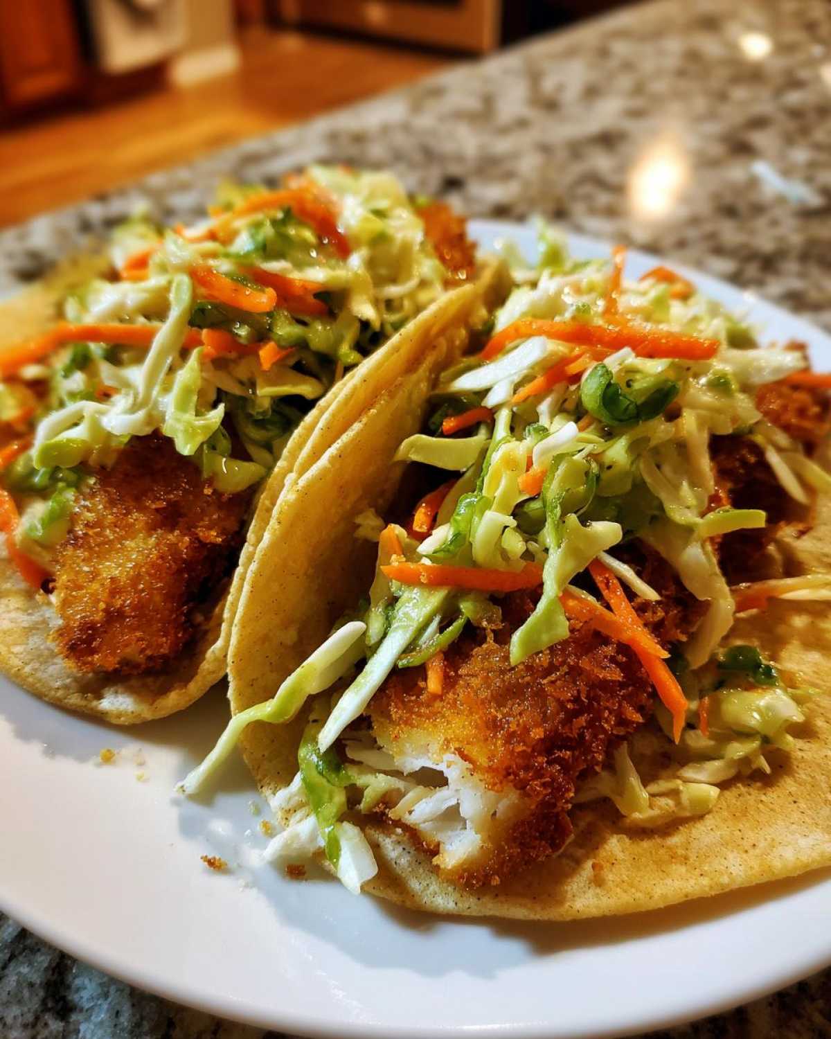 Two Crispy Baked Fish Tacos topped generously with lime slaw and served on a white plate.