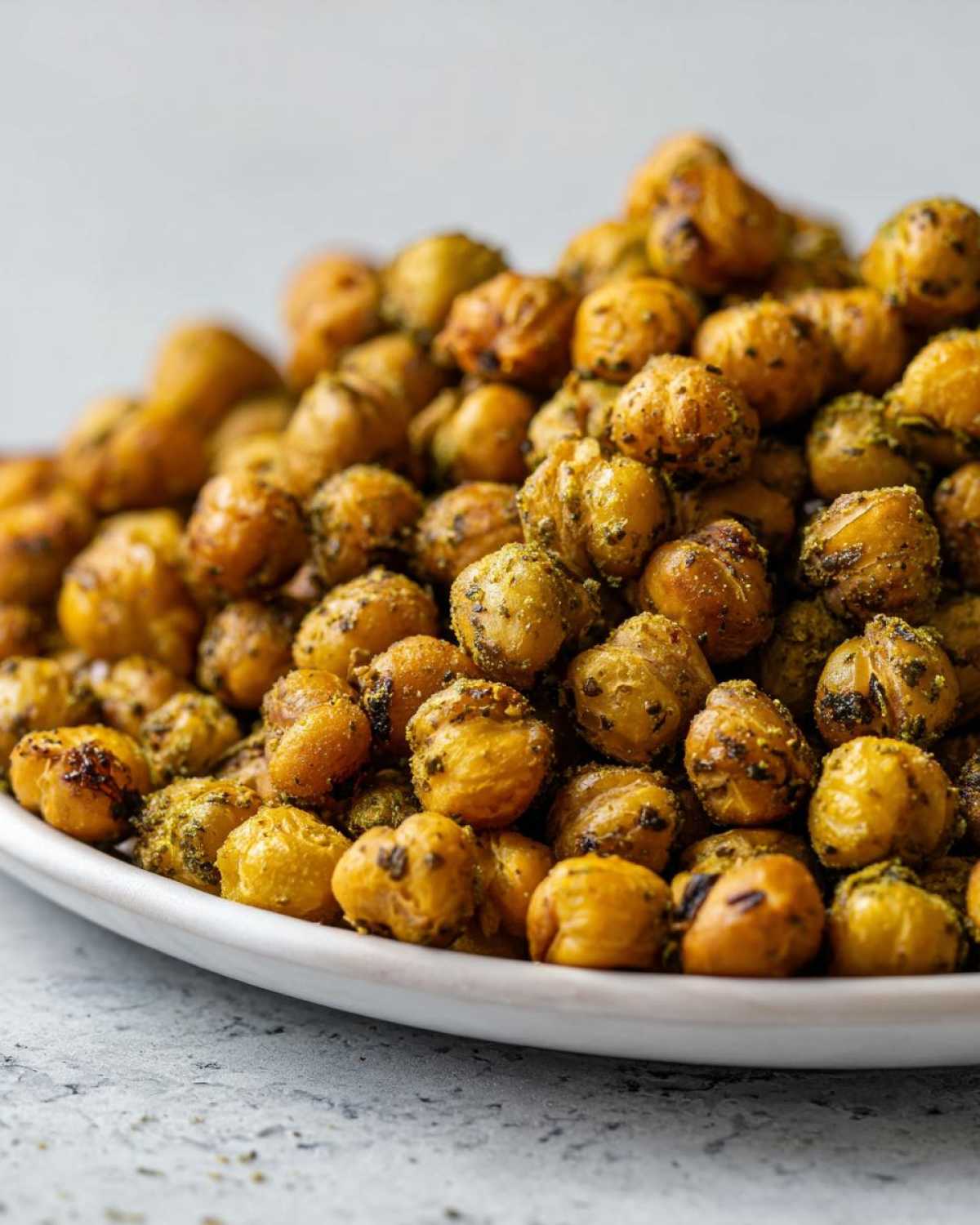 Close-up of a mound of golden, seasoned Crunchy Air Fryer Ranch Chickpeas piled high on a white plate.