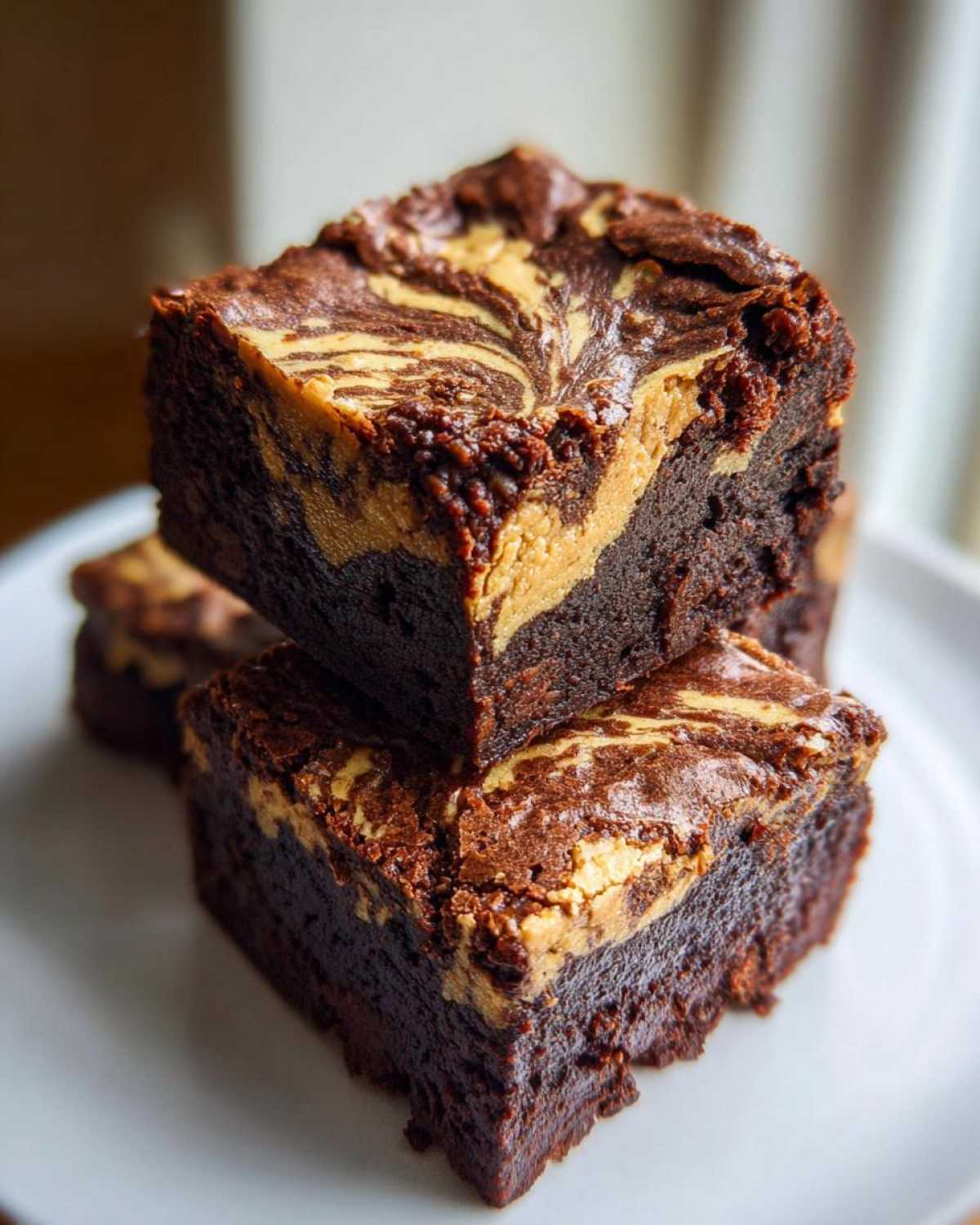 Two rich, fudgy Dark Chocolate Tahini Brownies stacked, showing a beautiful tan swirl pattern on top.