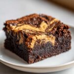 A close-up of a fudgy Dark Chocolate Tahini Brownies square with a visible tahini swirl on top.