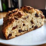 A close-up of a thick slice of Easy Irish Soda Bread with Buttermilk and Raisins on a white plate.