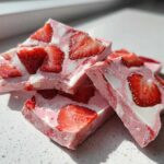 Close-up of several broken pieces of Frozen Strawberry Yogurt Bark, featuring pink yogurt swirled with white and topped with bright red strawberry slices.