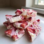 A stack of broken pieces of Frozen Strawberry Yogurt Bark showing white yogurt and bright red strawberry chunks.