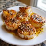 Five beautifully seared Garlic Butter Scallops with Lemon, glistening in butter sauce and topped with pepper.