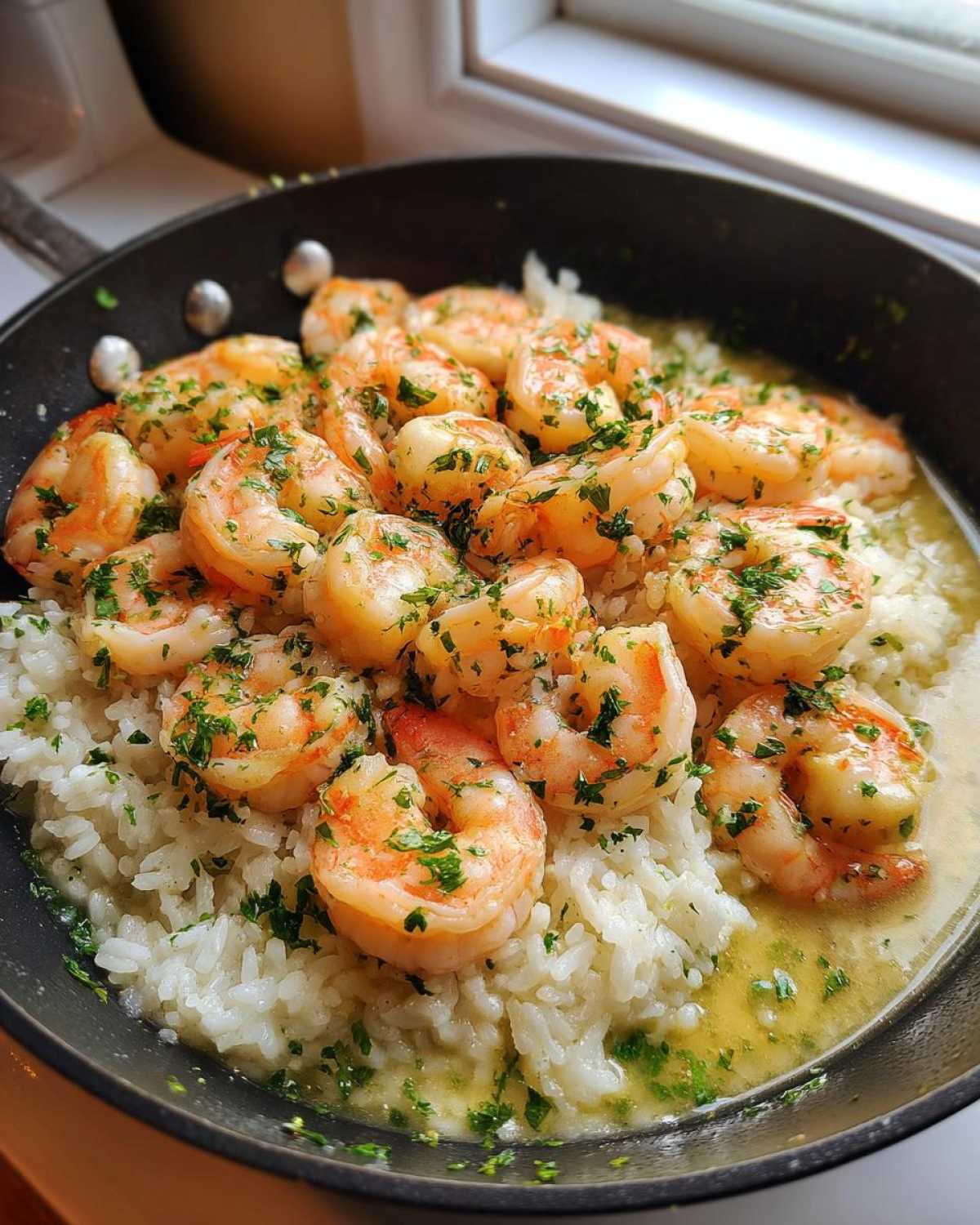 Close-up of plump, cooked shrimp served over white rice in a skillet, coated in garlic butter sauce and fresh parsley for Garlic Butter Shrimp and Rice Skillet.