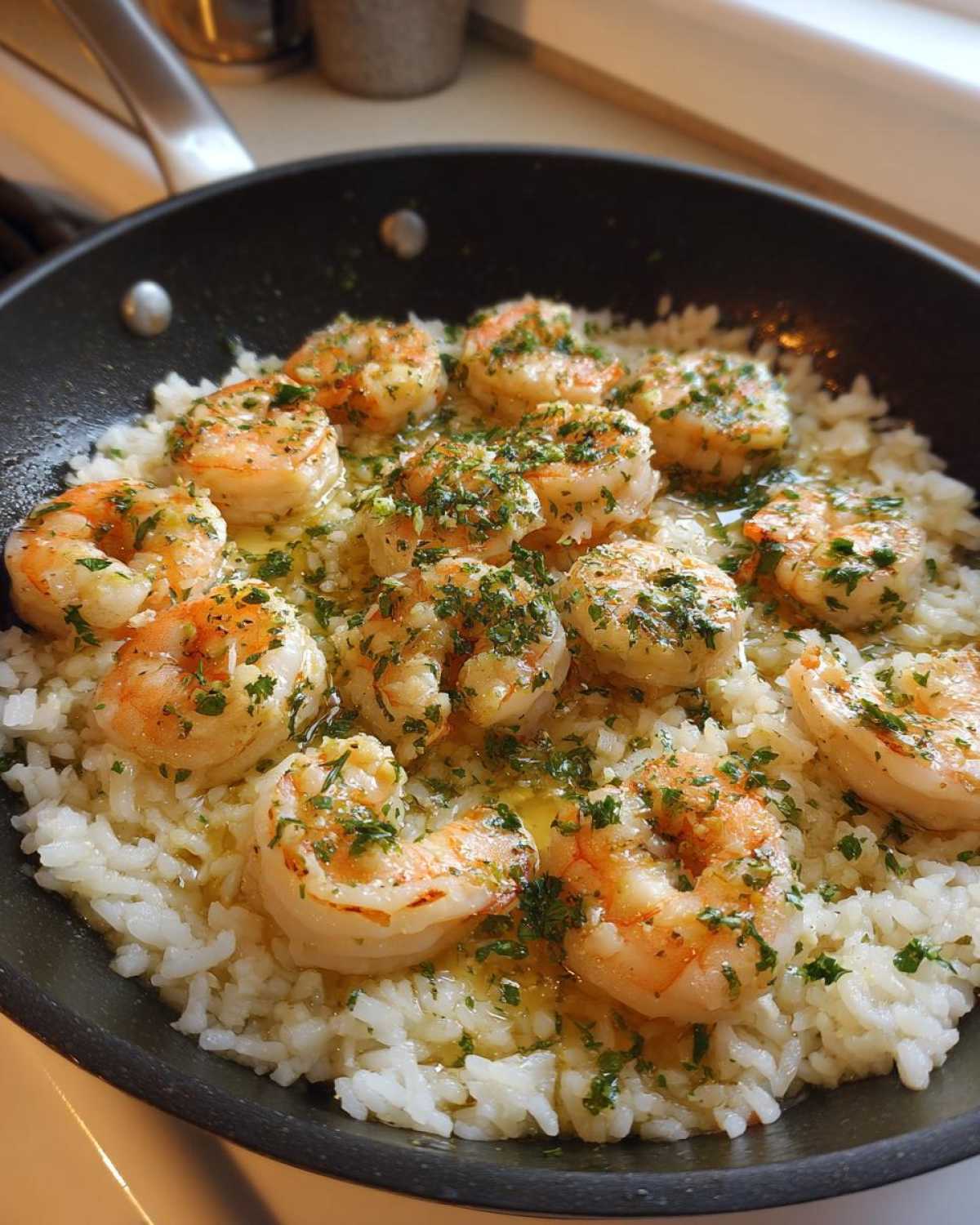 Close-up of succulent shrimp cooked in garlic butter sauce served over white rice in a black skillet, featuring fresh parsley.