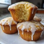 A stack of Glazed Lemon Poppy Seed Muffins, one on top broken open to show the soft interior.