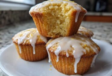 A stack of Glazed Lemon Poppy Seed Muffins, one on top broken open to show the soft interior.