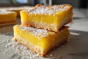 Two stacked slices of bright yellow Gluten-Free Lemon Bars with a shortbread crust, dusted with powdered sugar.