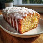A slice of moist Gluten-Free Lemon Coconut Cake topped with white glaze and shredded coconut flakes.