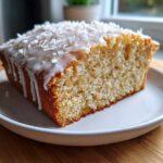 A close-up of a moist slice of Gluten-Free Lemon Coconut Cake topped with white icing and shredded coconut.