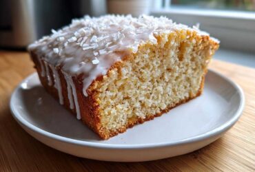 A close-up of a moist slice of Gluten-Free Lemon Coconut Cake topped with white icing and shredded coconut.