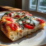 Close-up of a thick slice of Gluten-Free Margherita Pizza showing bubbly cheese, bright tomatoes, and fresh basil.