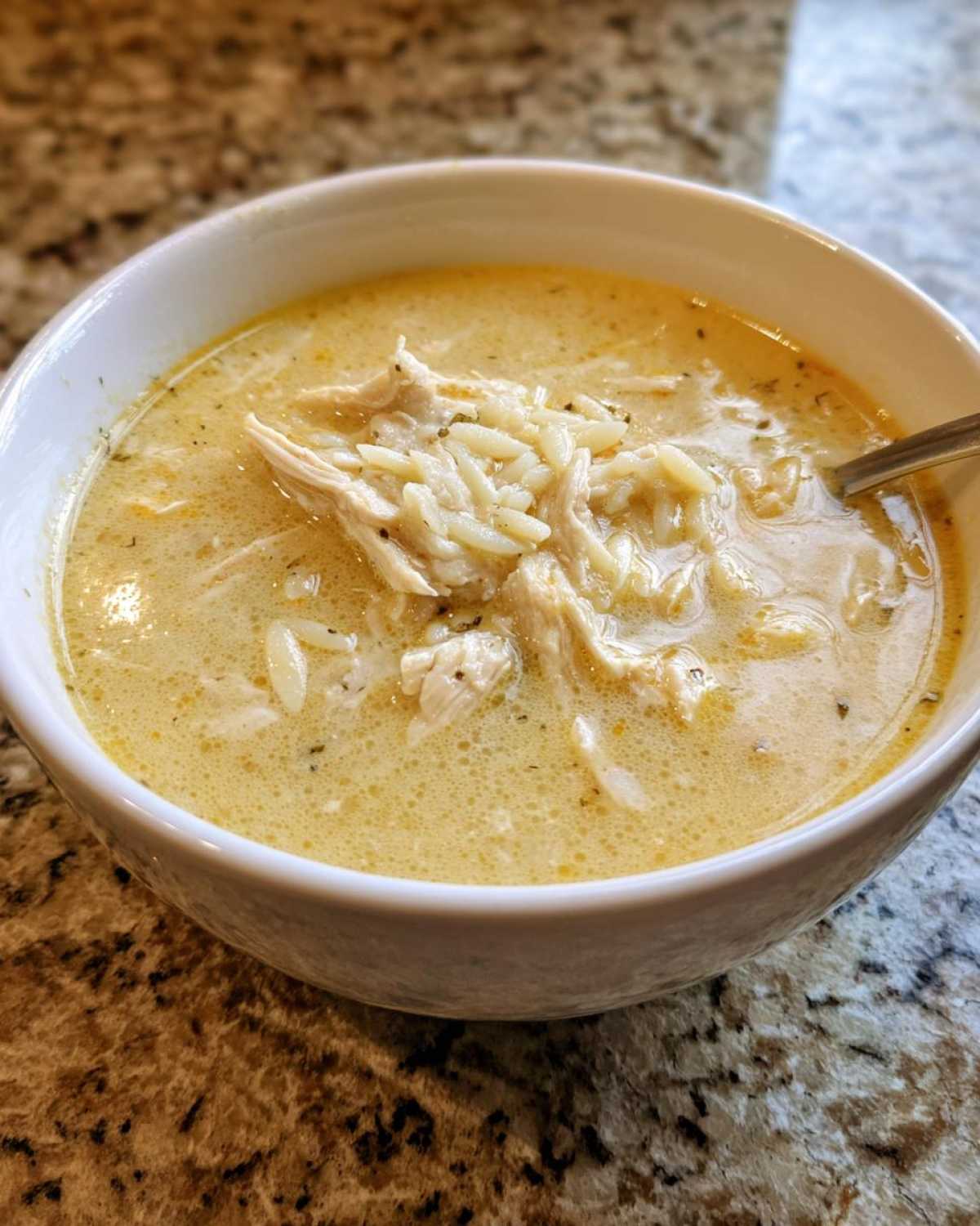 Close-up of a white bowl filled with creamy Greek Lemon Chicken Soup, featuring shredded chicken and orzo pasta.