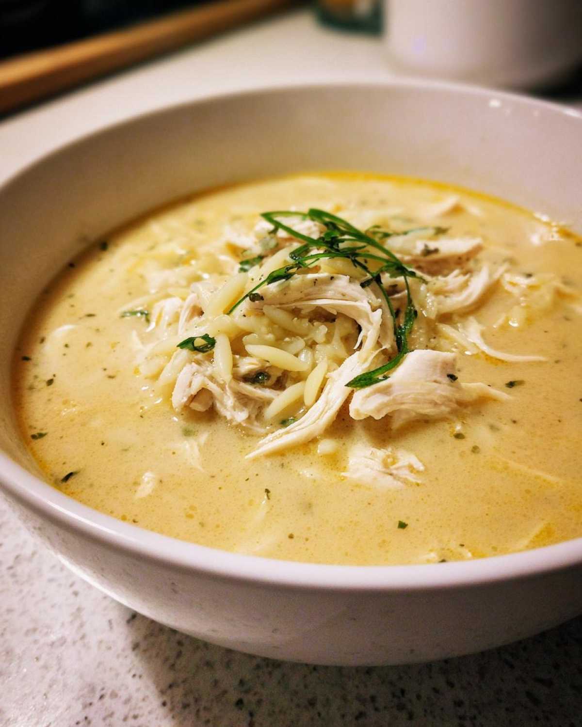 Close-up of a creamy bowl of Greek Lemon Chicken Soup topped with shredded chicken, orzo pasta, and fresh herbs.