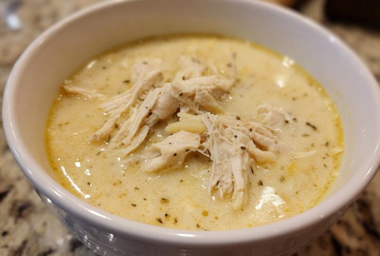 Close-up of a white bowl filled with creamy Greek Lemon Chicken Soup, topped with shredded chicken and herbs.