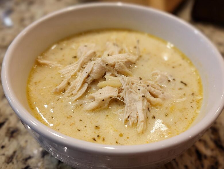 Close-up of a white bowl filled with creamy Greek Lemon Chicken Soup, topped with shredded chicken and herbs.