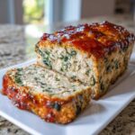 A sliced loaf of Healthy Turkey Spinach Meatloaf topped with a shiny, reddish-brown glaze, resting on a white platter.