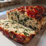 A slice cut from a Healthy Turkey Spinach Meatloaf, showing green spinach mixed into the turkey, topped with a shiny red glaze.