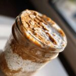 Close-up of High-Protein Peanut Butter Overnight Oats layered in a glass jar, topped with peanut butter swirls and rolled oats.