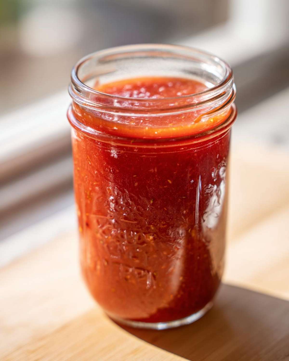 Close-up of a glass mason jar filled with bright red Homemade Strawberry Lemonade Concentrate.