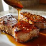 Close-up of a spoon drizzling thick, amber honey glaze over two perfectly seared Honey Glazed Ham Steak in the Skillet pieces.