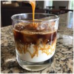 Caramel syrup being drizzled over an Iced Caramel Macchiato layered with milk, ice, and espresso.