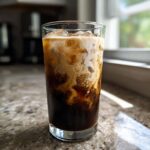 Close-up of an Iced Honey Almond Milk Latte showing the creamy almond milk swirling into the dark coffee over ice.