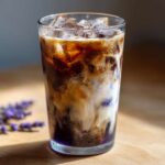 Close-up of a tall glass filled with an Iced Lavender Latte, showing layers of espresso, milk, ice, and purple syrup.