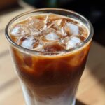 Close-up of a tall glass filled with an Iced Lavender Latte, showing layers of milk, espresso, and ice cubes.