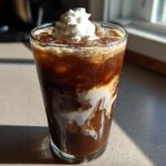 A tall glass of rich Iced Mocha with swirling cream and topped with whipped cream.