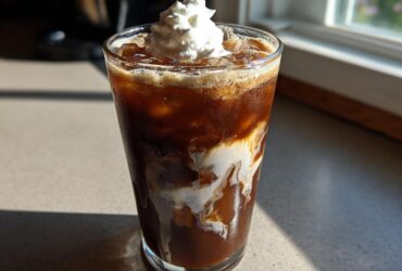 A tall glass of rich Iced Mocha with swirling cream and topped with whipped cream.