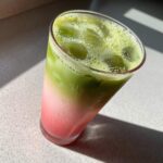 Close-up of a tall glass containing a layered Iced Strawberry Matcha Latte with bright pink and green layers over ice.