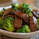 Close-up of tender beef slices coated in savory sauce mixed with bright green broccoli florets in a white bowl, showcasing Instant Pot Beef and Broccoli.