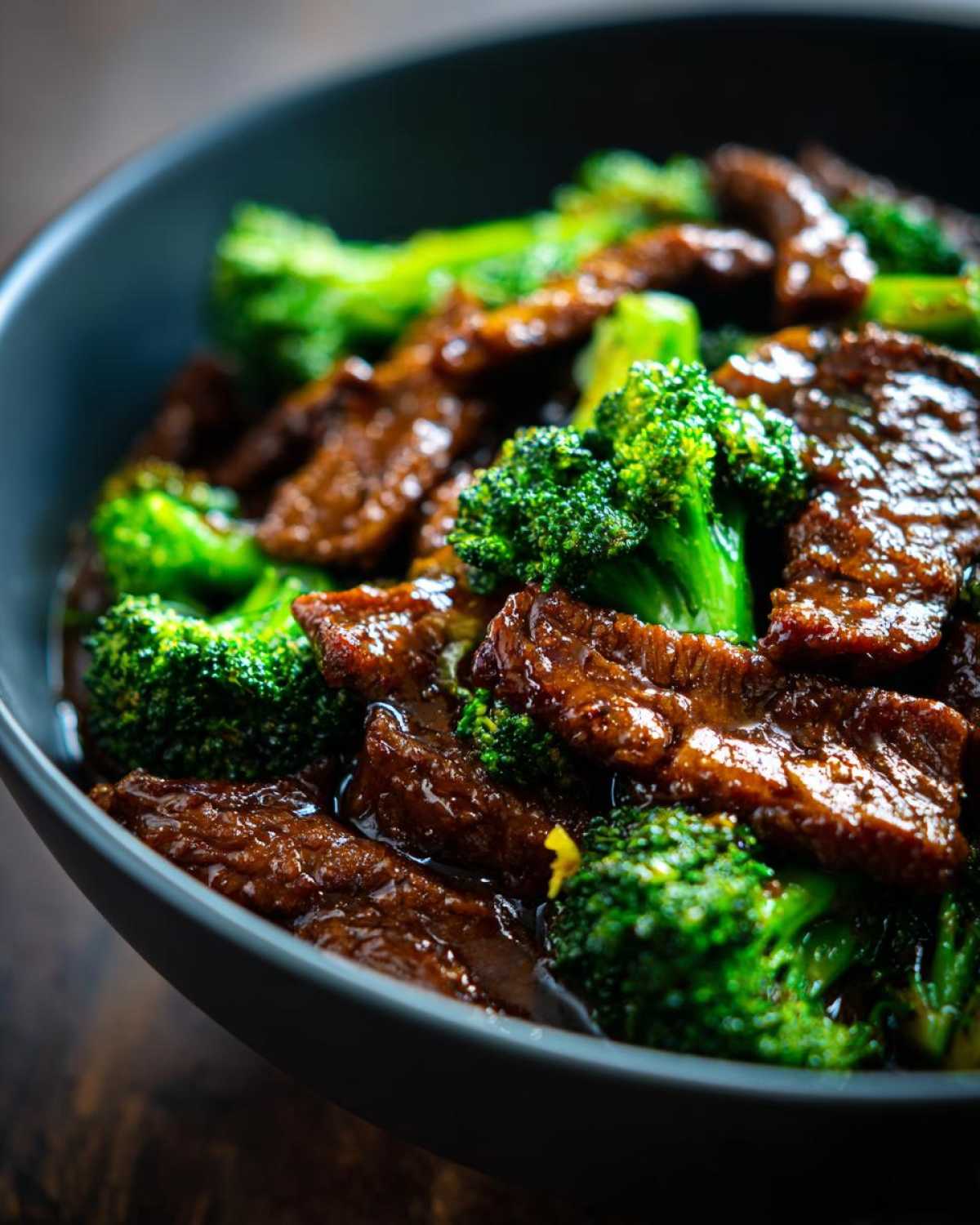 Close-up of tender beef slices coated in savory sauce mixed with bright green broccoli florets in a dark bowl, showcasing Instant Pot Beef and Broccoli.