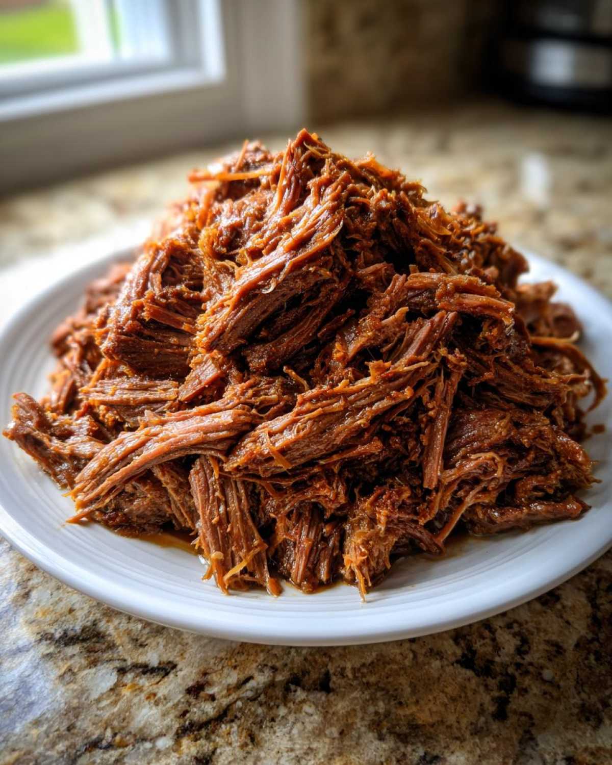 A large mound of perfectly shredded, saucy Instant Pot Beef Barbacoa piled high on a white plate.