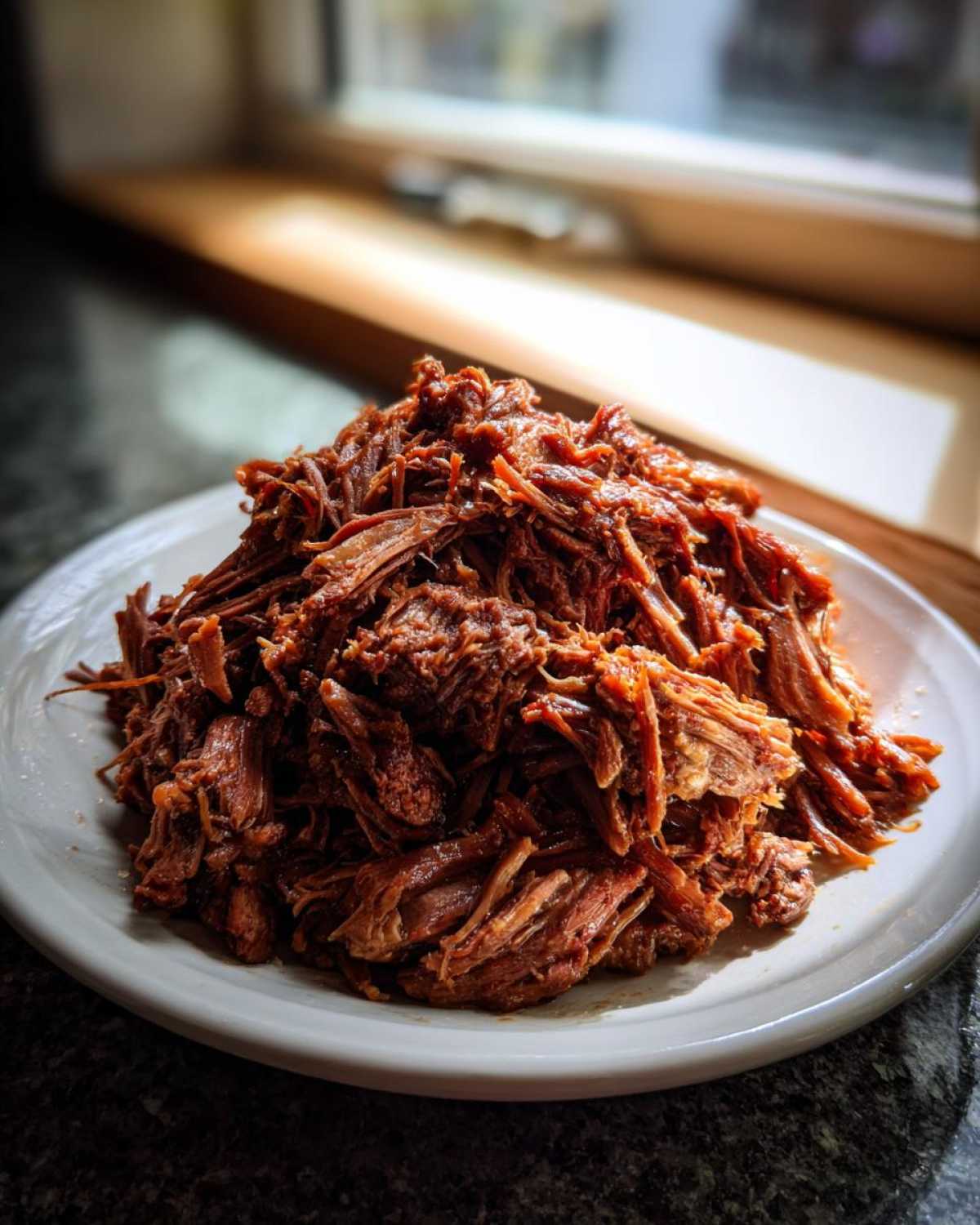 A mound of richly seasoned, shredded Instant Pot Beef Barbacoa piled high on a white plate.