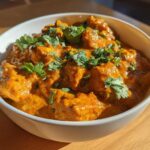 A close-up of vibrant orange Instant Pot Butter Chicken garnished with fresh cilantro in a white bowl.