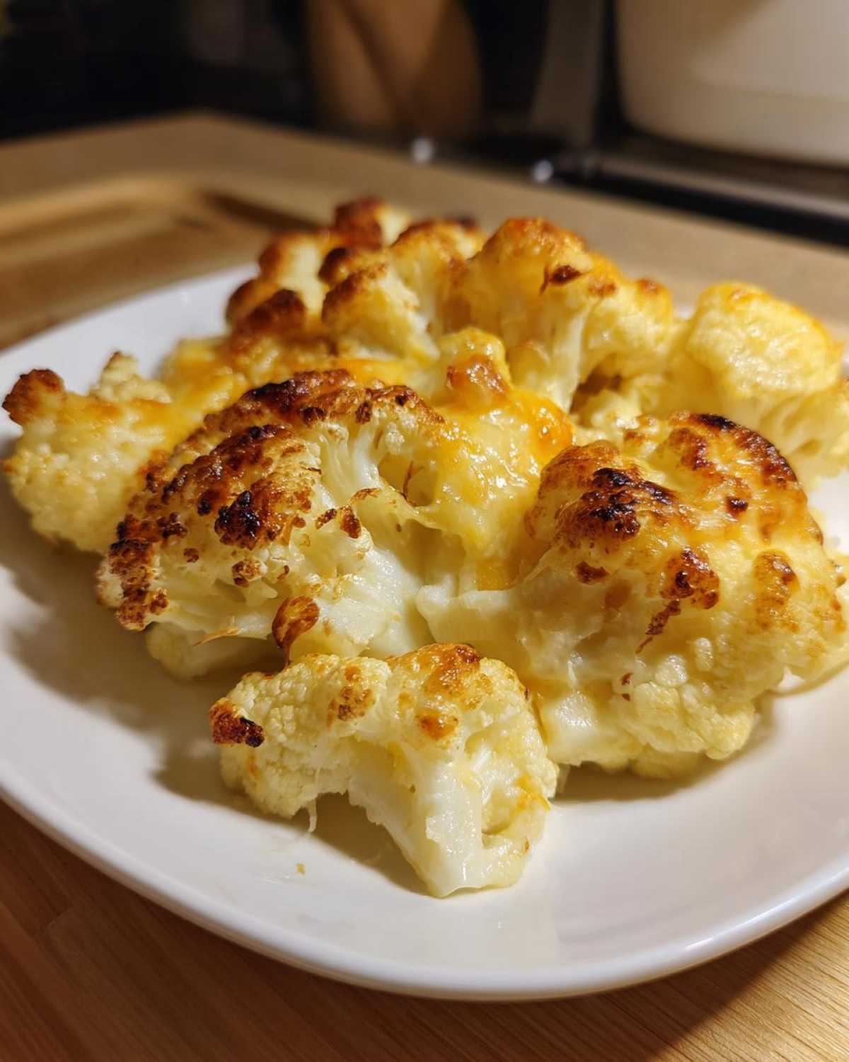 A close-up of cheesy Keto Cauliflower Mac and Cheese florets with a golden-brown, baked top on a white plate.