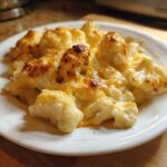 A close-up of cheesy Keto Cauliflower Mac and Cheese with browned cheese topping on a white plate.