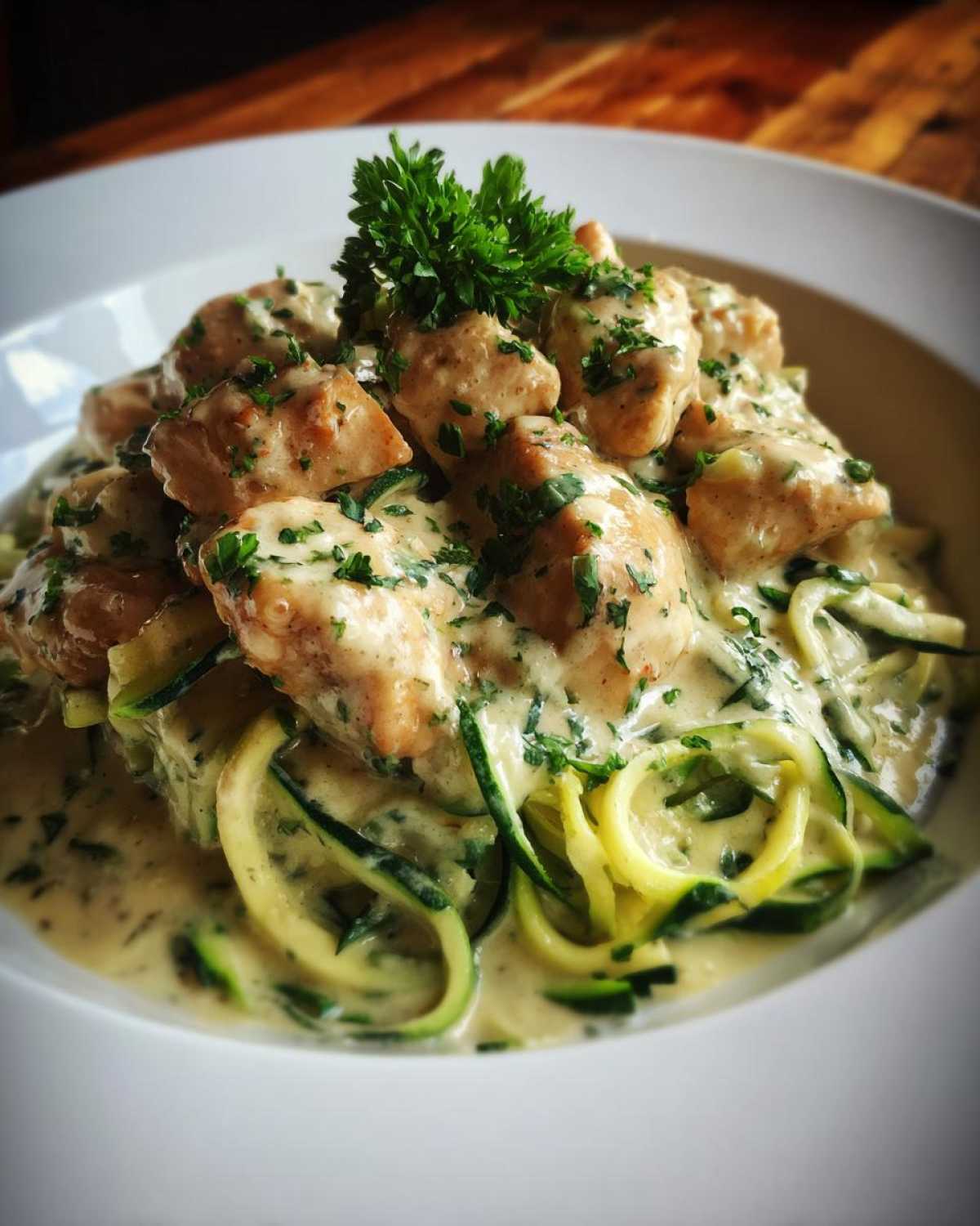 A bowl of Keto Chicken Alfredo featuring creamy sauce, sautéed chicken pieces, and zucchini noodles (zoodles), garnished with parsley.