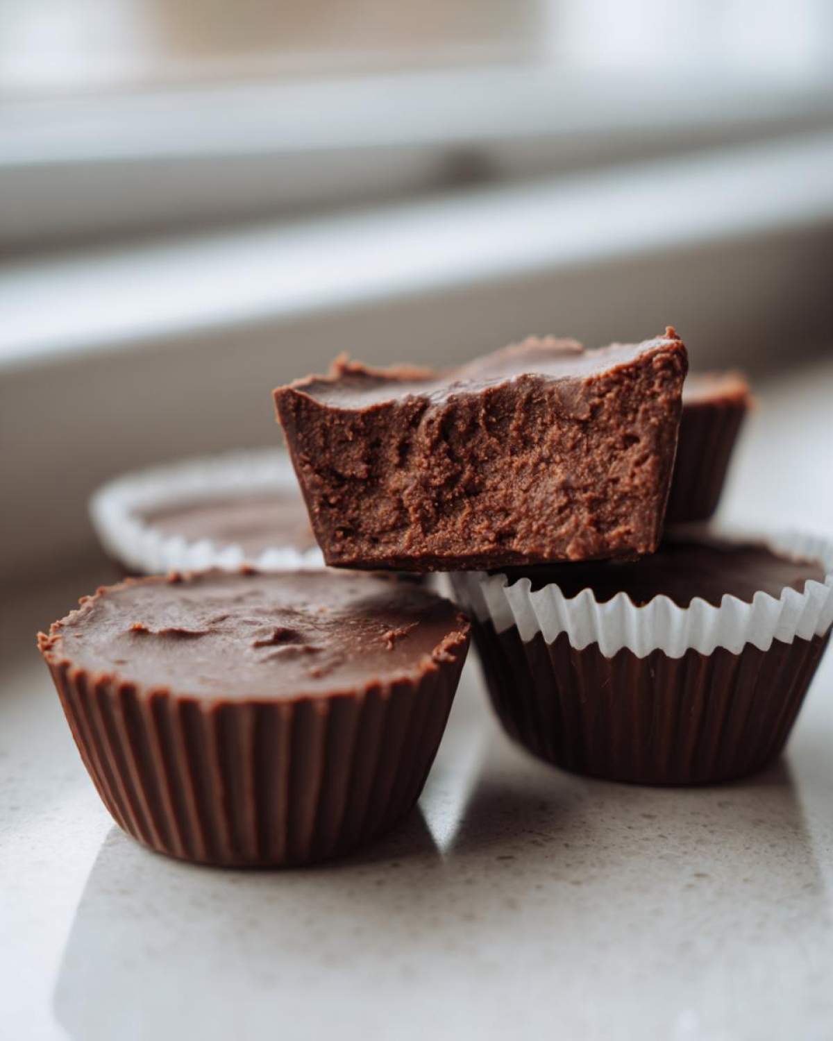 A stack of rich, dark chocolate Keto Chocolate Peanut Butter Fat Bombs, one cut open to show the dense texture.