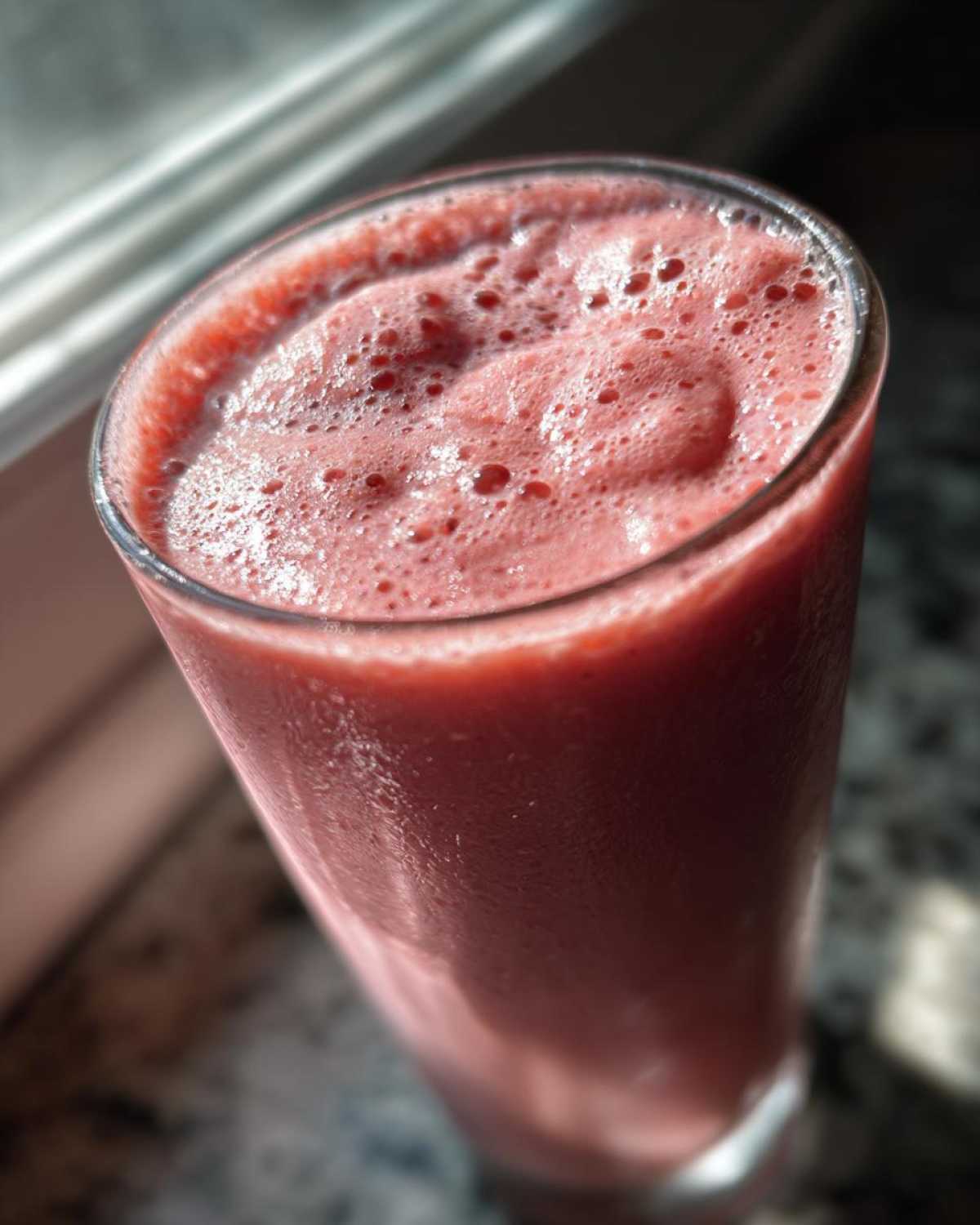 Close-up of a tall glass filled with a thick, pink Keto Strawberry Cheesecake Smoothie, showing frothy bubbles on top.