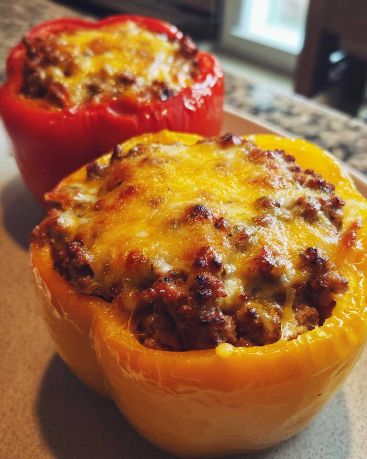 Two colorful bell peppers stuffed with seasoned meat and topped with melted, browned cheese, representing Keto Taco Stuffed Peppers.