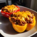 Two halves of Keto Taco Stuffed Peppers, one yellow and one red, topped with melted cheddar cheese.