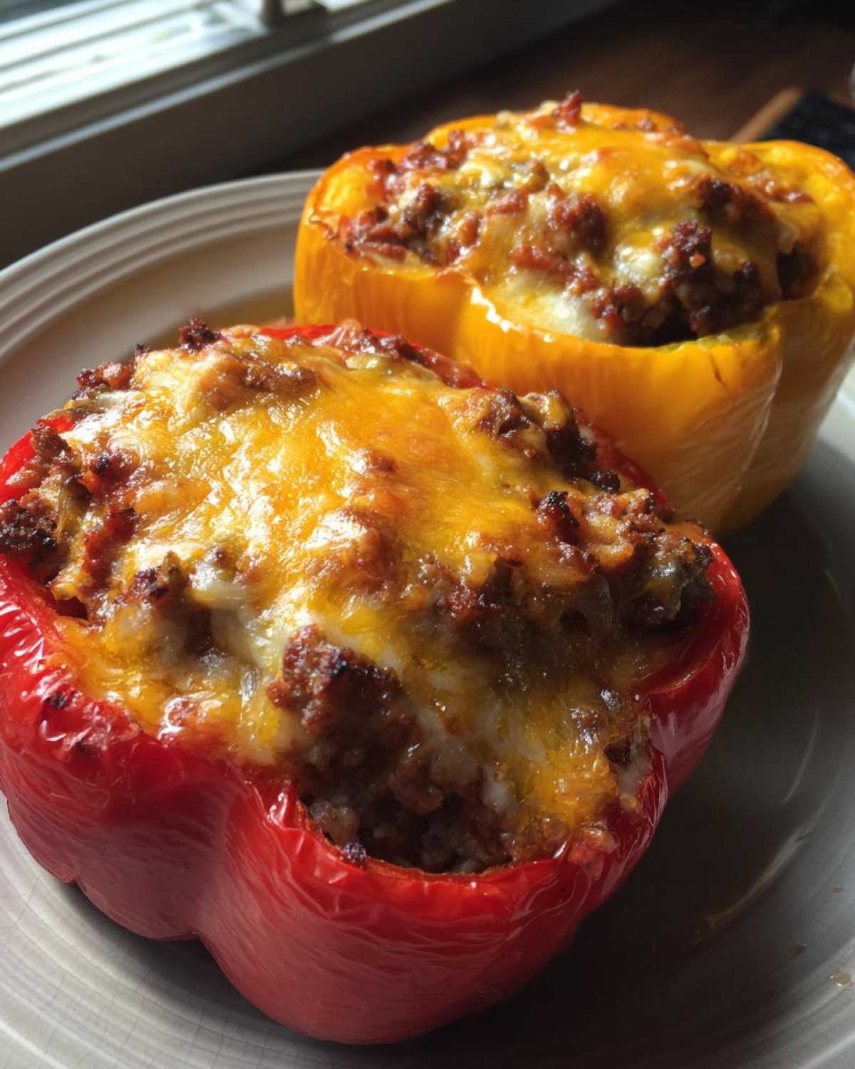 Two Keto Taco Stuffed Peppers, one red and one yellow, topped with browned, melted cheddar cheese.