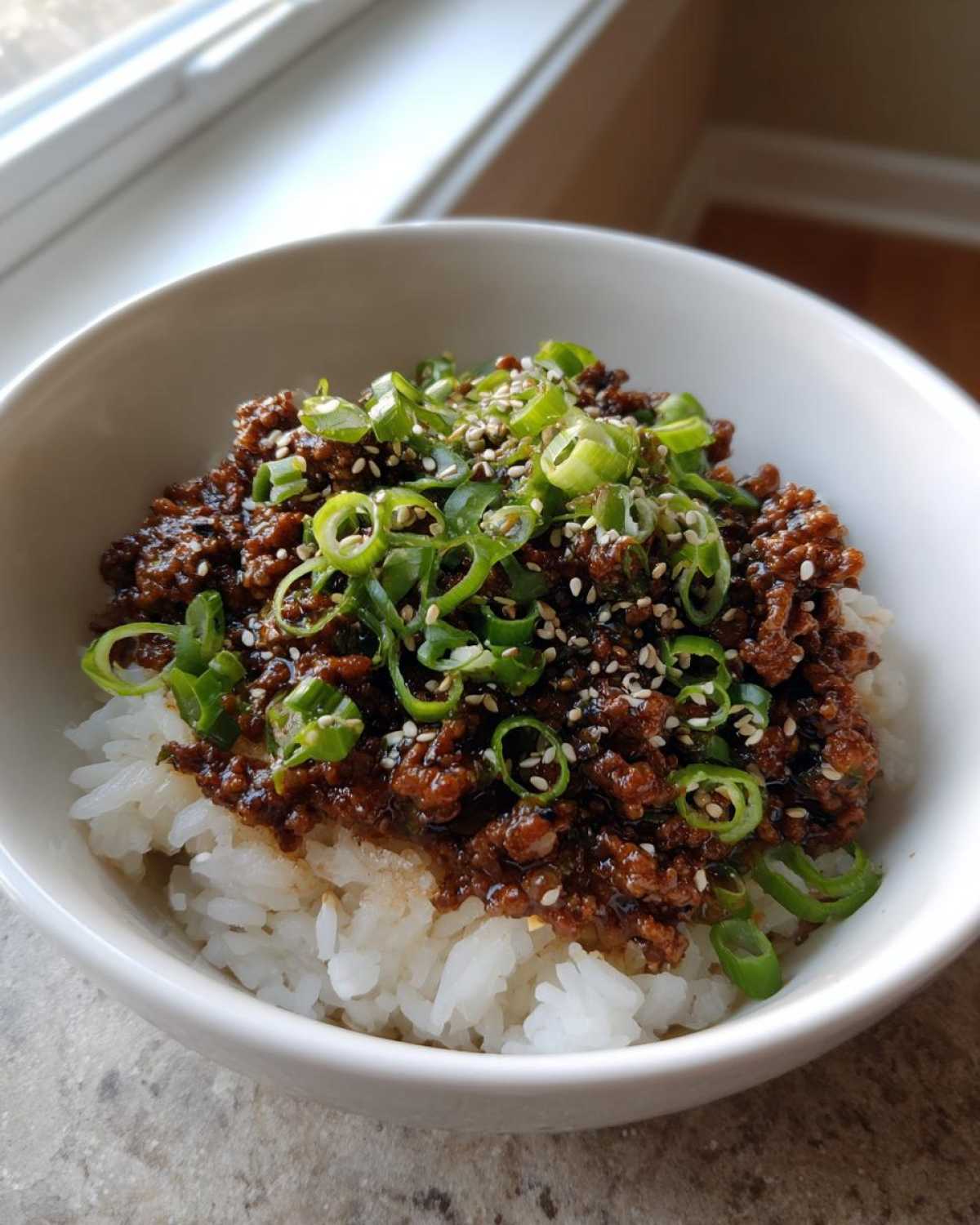 A close-up of Korean Ground Beef Bulgogi Bowls featuring savory ground beef over white rice, topped with sliced green onions and sesame seeds.