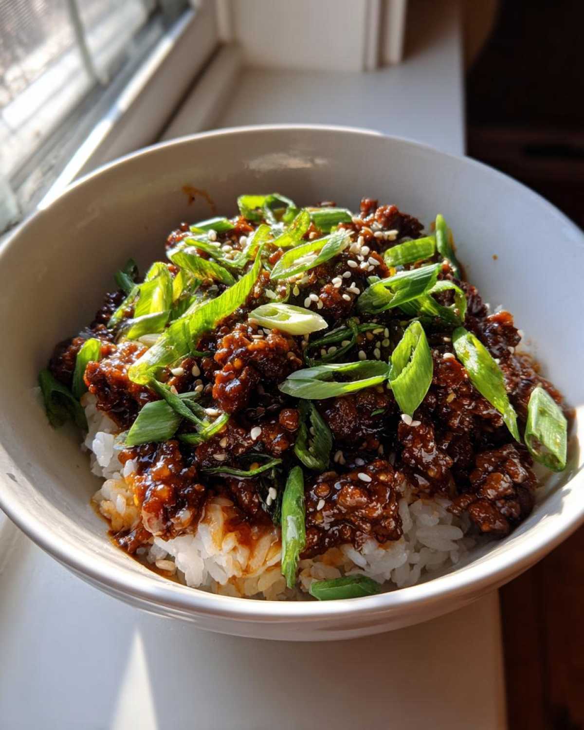 A close-up of Korean Ground Beef Bulgogi Bowls served over white rice and topped with fresh green onions and sesame seeds.